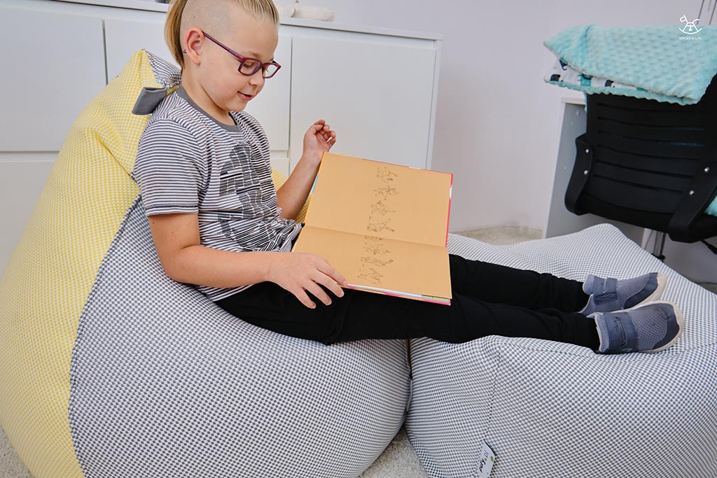 chłopiec czyta książkę na jasnych pufach w swoim pokoju